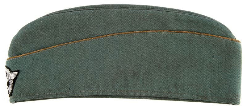 WWII SCHUTZPOLIZEI OVERSEAS CAP: This cap is constructed of green wool with machine woven police eagle & wreath on front against a black background. It has gold piping. Interior is fully lined in grey rayon/cotton twill. Size 57 in v