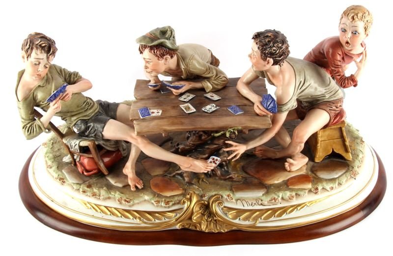 BRUNO MERLI THE CARD CHEATS PORCELAIN FIGURES: Bruno Merli ?The Card Cheats? with maker?s mark ?King?s?. Measures approximately 12 by 24 inches and stands 10 inches high. Minor tip chips to several points and a card on the table is cracked. Overal