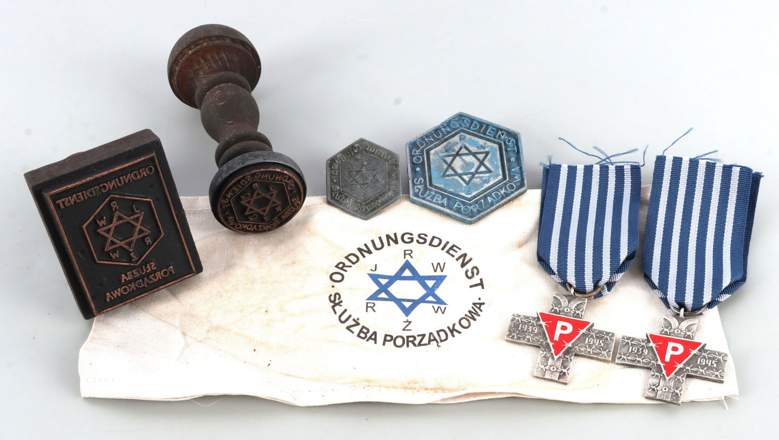 WWII GERMAN THIRD REICH WARSAW GHETTO ITEMS LOT 7: A lot of seven items related to the Warsaw Ghetto. 1) Armband. 2) Hat badge. 3) Breast badge. 4) Hand stamp. 5) Hand stamp. 6) Auschwitz cross. 7) Auschwitz cross. Unauthenticated, sold as is.