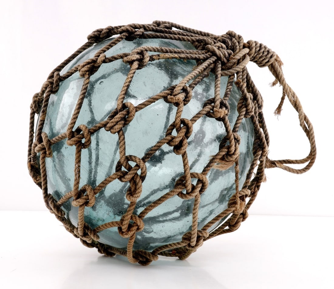 MID 20TH CENTURY JAPANESE FISHING GLOATS IN NET: A Japanese fishing float, wrapped in knotted netting, likely mid-20th century. This float was recovered from a beach on Iwo Jima from the 1960s, per previous owner. 9 inches tall, 10 inches diameter. 
