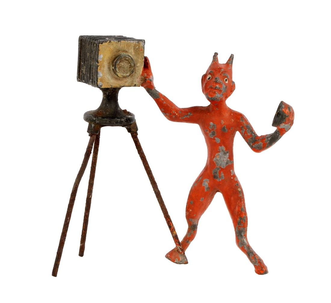 DEVIL WITH A TRIPOD CAMERA HEYDE CAST LEAD TOY: Unusual painted cast lead figurine. A devil or lesser imp removing the lens cap of a tripod camera. Pre-war, probably George Heyde of Dresden. Height 3 inches. Width 3 inches. Good condition, retains