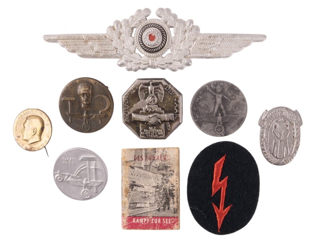 WWII GERMAN REICH COLLECTION OF TINNIES LOT OF 9: A collection of nine small items from the German Third Reich. Six tinnies, one visor cap badge, a patch, and a small booklet about naval warfare.
