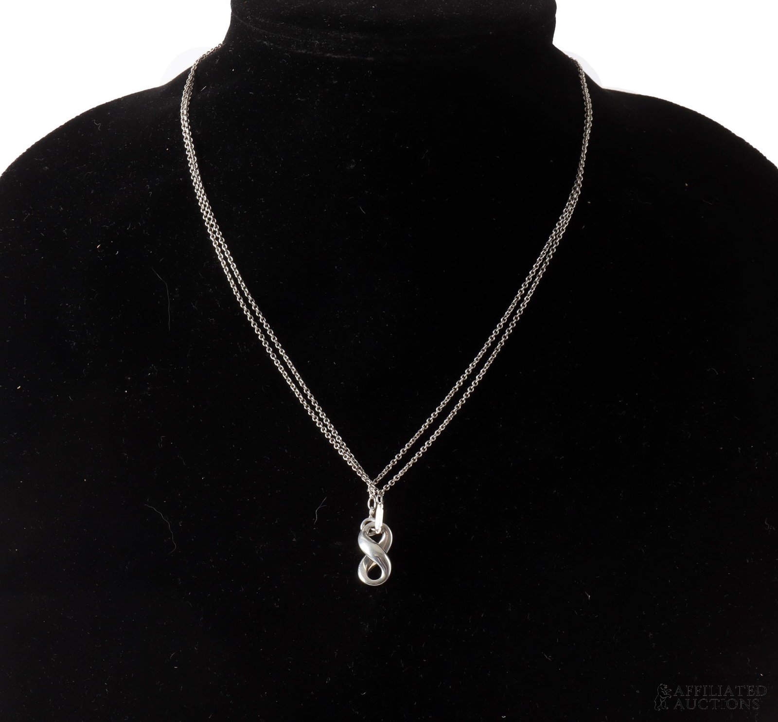 Tiffany Sterling Silver Infinity Pendant Necklace: A sterling silver Infinity pendant necklace by Tiffany & Co. The piece features a stylized infinity symbol centered along a looped double-strand chain, finished with a secure spring ring clasp. Stampe