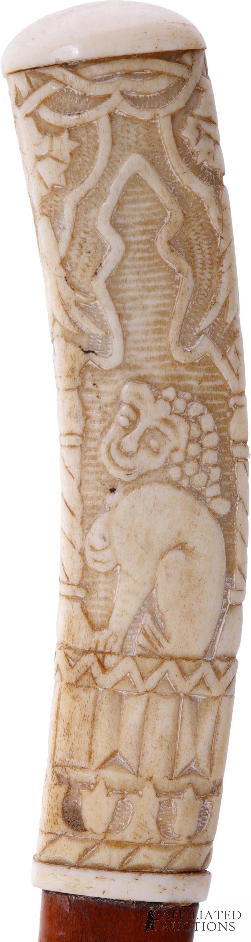 African Scene Walking Stick Cane Bone: A walking stick with a bone handle, carved to depict a sitting man in a turban, an elephant, and a lion amidst floral scenery. Bamboo shaft. Brass ferrule. Late nineteenth century. 32 inches.