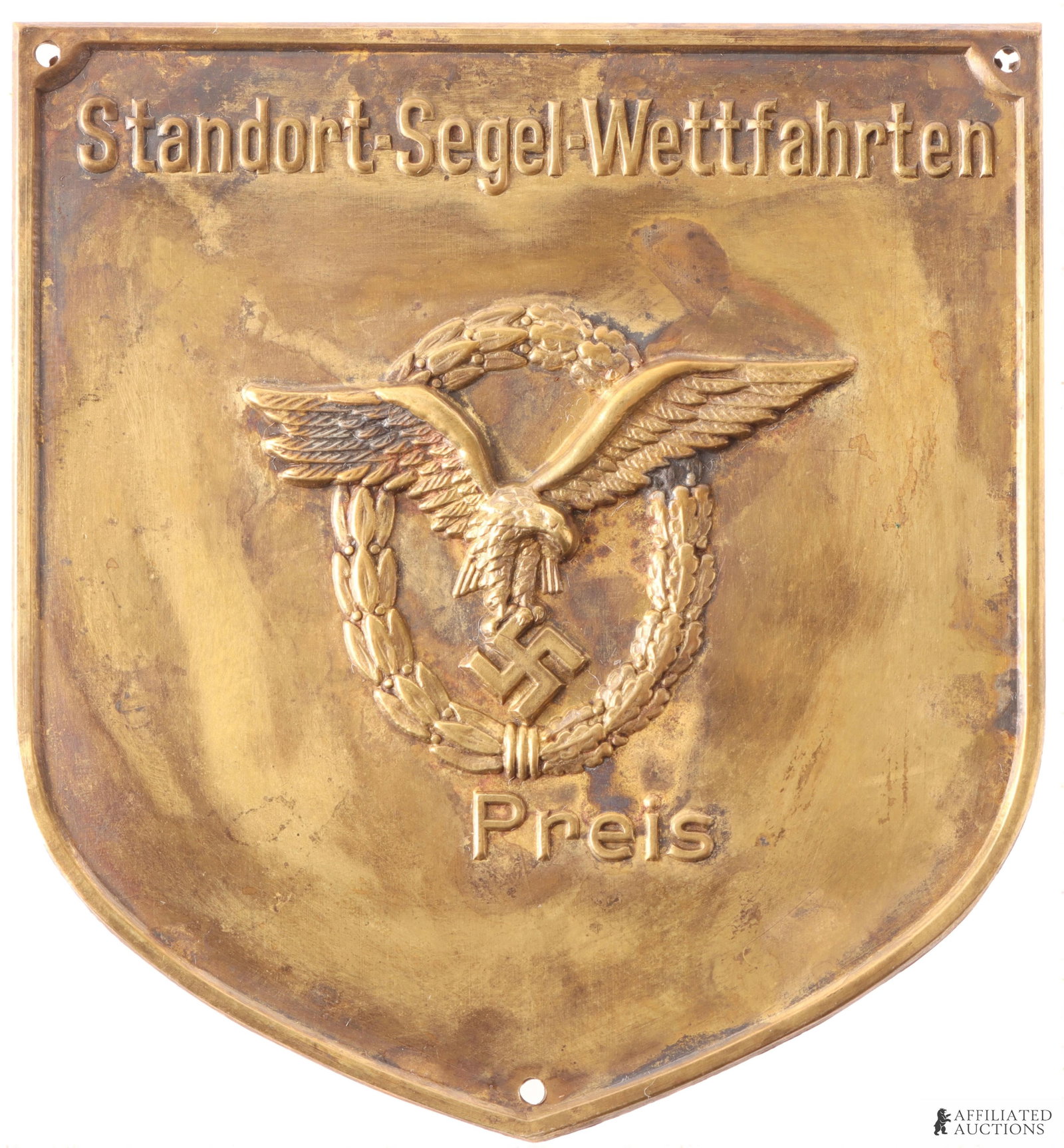 Luftwaffe Plaque WWII German Third Reich: Brass construction. Stamped. It features a pilot/observer badge embossed with words "Standort-Segel-Wettfahrten." It measures 2 5/8 x 2 3/8 inches. | This lot has a reserve.