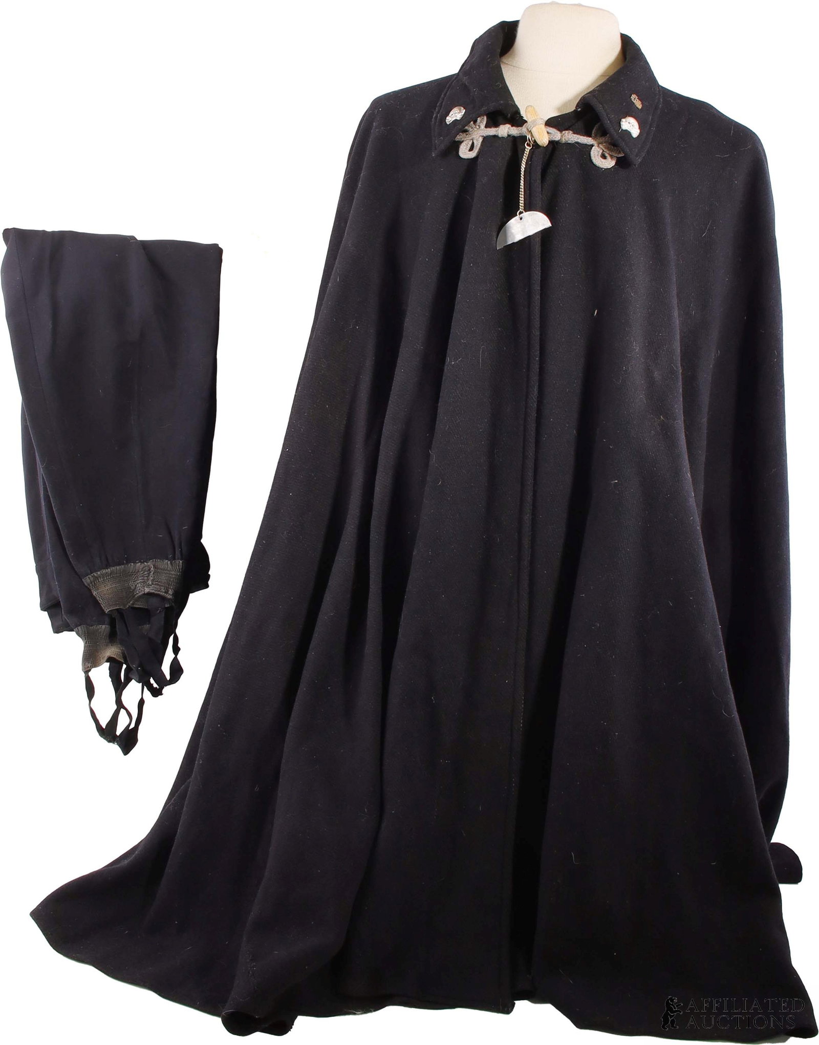 WWII Wool SS Cape with Trousers German Third Reich: A black wool SS cape with the top half of a WWII-era German military dog tag (stamped 'ObFr. Si. Po. It.') and a pair of black trousers with stirrups. The cape has a Totenkopf pin on either side of th