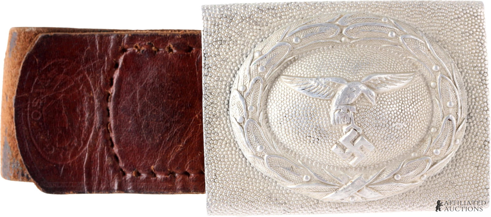Luftwaffe Flying Eagle Belt Buckle WWII German: A belt buckle for the Luftwaffe of the German Third Reich. Shows a flying eagle clutching a swastika. Pebbled aluminum construction. Leather tab intact with Osang stamp. 2.5x1.75 inches.
