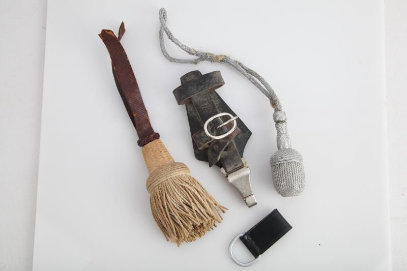 ASSORTED WWII GERMAN EDGED WEAPON ACCOUTREMENTS: Four accoutrements to WWII German edged weapons. Portepee with some fraying to cord, sword knot with portion of strap missing, belt loop hanger, and repro SS hanger.