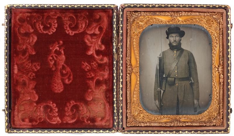 CIVIL WAR AMBROTYPE OF A GEORGIA CONFEDERATE: Sixth-plate Civil War Ambrotype of an unnamed CSA Georgia infantryman. Soldier is donning simple nine button grey frock coat and typical accoutrements of a Georgia Confederate soldier. Mounted in embo