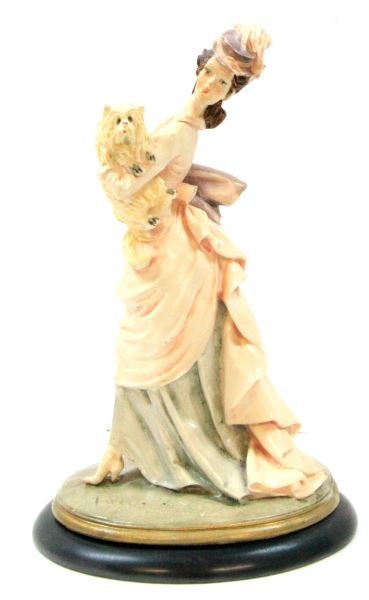 SIGNED BRUNO MERLI FIGURINE LADY CARRYING DOG: 12 inches tall by 7.5 inches with oval base. Victorian lady carrying small dog in her arms. Signed near foot. Very good condition.