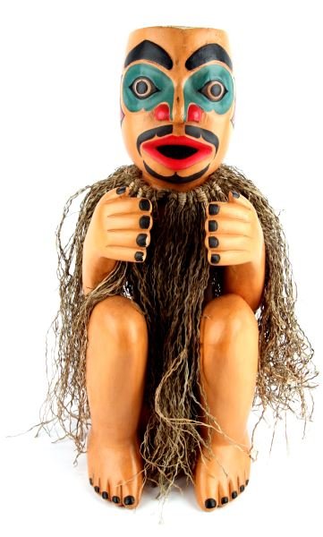 CONTEMPORARY HAIDA WOOD CARVED TOTEM FIGURE: Contemporary Haida-style wood carved totem figure of crouching man with hand gesture. Bright green, red and black paint and raffia dress. Looks to be emanating bird spirit. Measures 22 inches tall by 