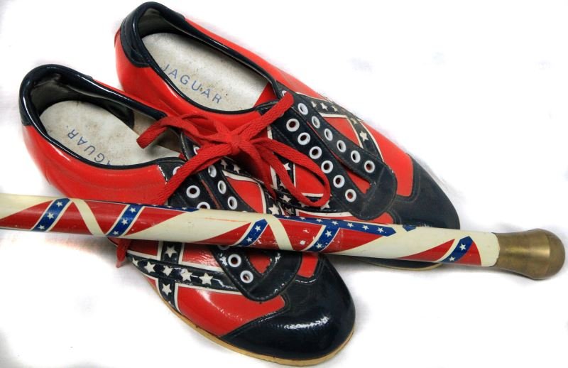 REBEL FLAG SHOES AND WALKING CANE: Walking cane and shoes featuring rebel flag design. Shoes are stamped with three different sizes (9, 8, and 10.5) but appear to be men’s size 8. Inside of the shoes appear to be worn (removable Jagu
