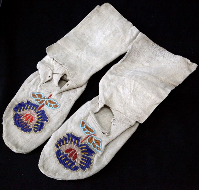 NATIVE AMERICAN BEADED BRAIN TANNED HIDE MOCCASINS: Reservation era possibly Chippewa, brain tanned leather hide high top moccasins. Floral bead work to front tops. Laces are absent. Very good condition. Rough rawhide soles are about 8.5 inches long.