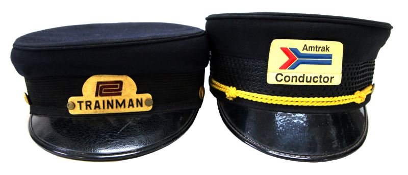 SET OF TWO TRAIN CONDUCTOR VISOR CAPS: Amtrak and Pennsylvania Railroad caps. Both with original sweatbands and metal emblems for the railway company. The Pennsylvania Railroad cap has side buttons with emblem. The cap is circa 1960's and 