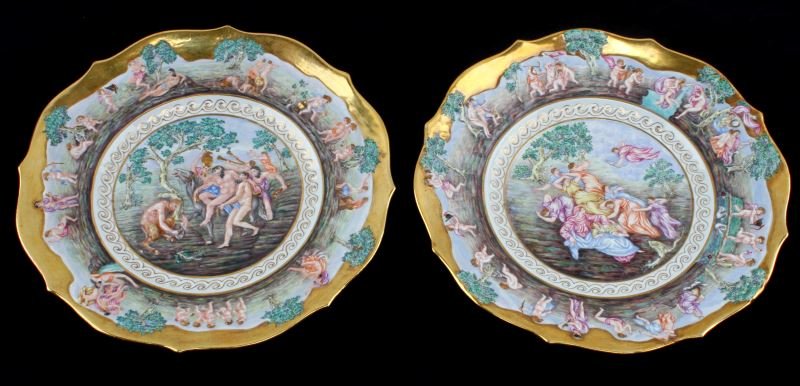 CAPODIMONTE CLASSICAL PLATE LOT OF TWO 8.5 INCHES: Lot of two Capodimonte hand painted porcelain plates with low relief figural details. The first plate in the lot has a central scene that appears to depict Bacchus and his followers. The rim has cupid