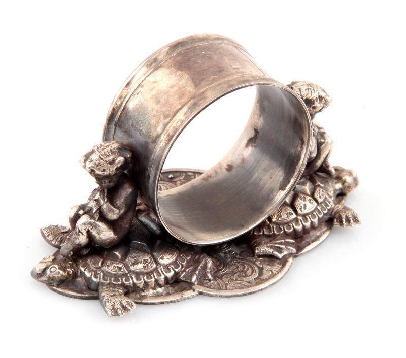 SILVER PLATE FIGURAL NAPKIN RING PUTI AND TURTLES: Antique silver plate figural napkin ring. The ring stands on a base of sea turtles and floral motifs. Two puti figures sit above a the sea turtles, and lean against the ring. Highly detailed. No appar