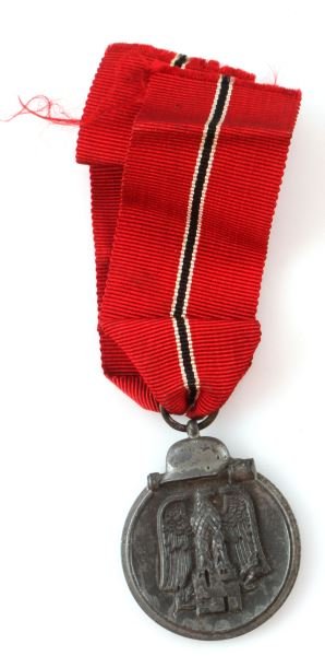 WWII THIRD REICH GERMAN EASTERN FRONT MEDAL: A German Eastern front medal with original red ribbon. Features a Parteiadler eagle under a helmet and grenade motif. In good condition with some plating missing.