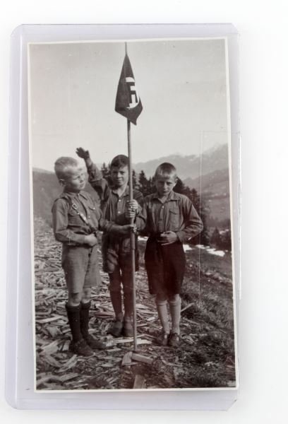 WWII HITLER YOUTH PERIOD PHOTOGRAPH GERMAN: Three young German boys in landscape holding party flag. World War II era photograph. The reverse has illegible writing. Overall very good condition. 2 by 3.75 inches.
