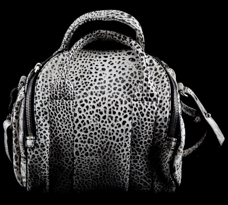 ALEXANDER WANG ROCKY SLING PEBBLED PURSE: Alexander Wang "Rockie" sling in pebbled black and white leather. Has top zipped opening, studded bottom, and two hidden pockets on one side of the exterior. Appears unused. Contains Alexander Wang pa