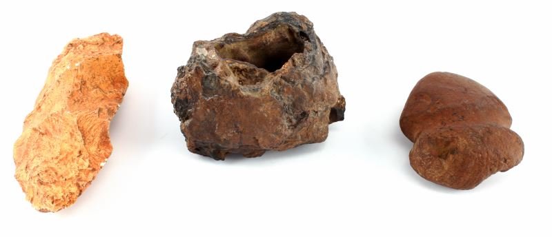 NATIVE AMERICAN STONE TOOLS W GROOVED AXE HEAD: Native American mixed stone tool group of three. Includes: matte smooth red stone grooved axe (3.5 inches), orange colored flint tool (almost 7 inches), and a darker molten rock with opening (4.5 by 3