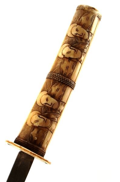 JAPANESE BONE GRIP AND SCABBARD SOUVENEIR DAGGER: A souveneir katana dagger with ccarved bone grip, tsuba and scabbard. Carved bone pieces show a repeating pattern of two faces facing each other. The blade is marked near the hilt and it is in very go