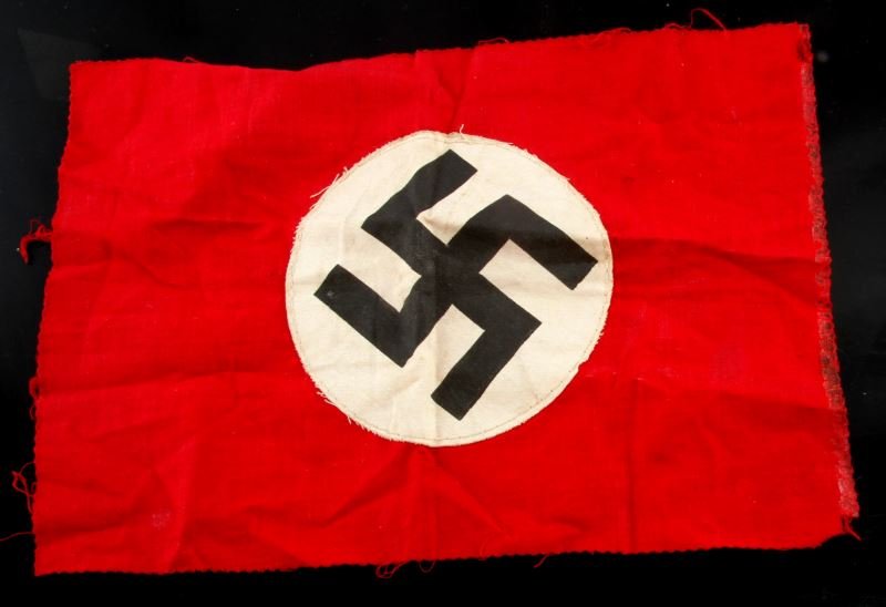 WWII THIRD REICH SMALL SWASTIKA NSDAP FLAG: A double-sided flag or part of a flag with a stitched-on mobile swastika on a white circle on a red field. Edges have been cut with pinking shears, and one edge shows signs of adhesive. Measures 11 by