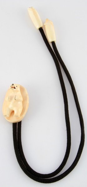 ALASKAN J. IYAHUK IVORY POLAR BEAR BOLO TIE: An ivory bolo tie in the shape of a polar bear. Signed "Joseph Iyahuk". The slide depicts a full length polar bear. The tips depict polar bear heads. In excellent condition.