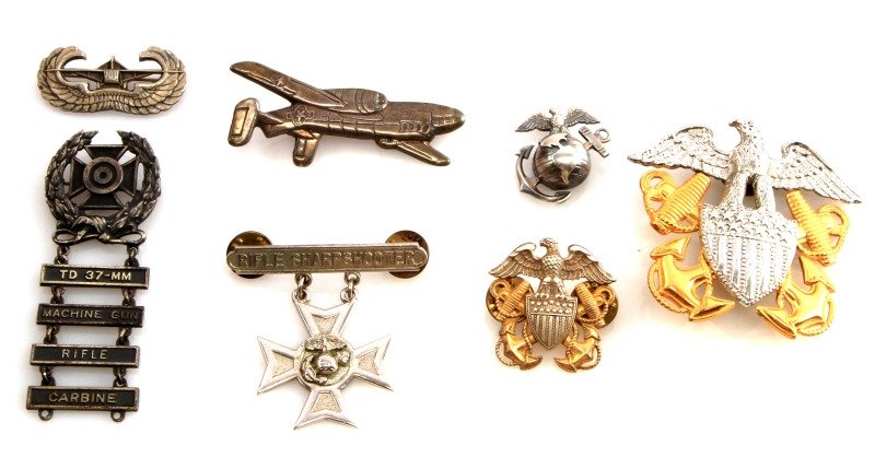WWII US NAVY & MARINE CORP STERLING BADGE LOT OF 7: Includes a Navy sterling stamped Cod aircraft pin measuring 3 inches. Naval office full size visor and garrison cap insignia in sterling, the lesser by Balfour. WWII sterling USMC collar EGA. WWII ste
