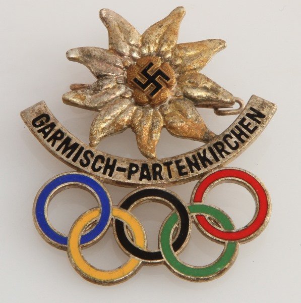 WWII WINTER OLYMPICS BADGE GARMISCH PARTENKIRCHEN: German World War II 1936 Winter Olympics Badge with edelweiss flower and the Olympic rings. The front reads "Garmisc-Partenkirchen", the reverse is marked ‘Annestsberger Munchen’ around the pin. M
