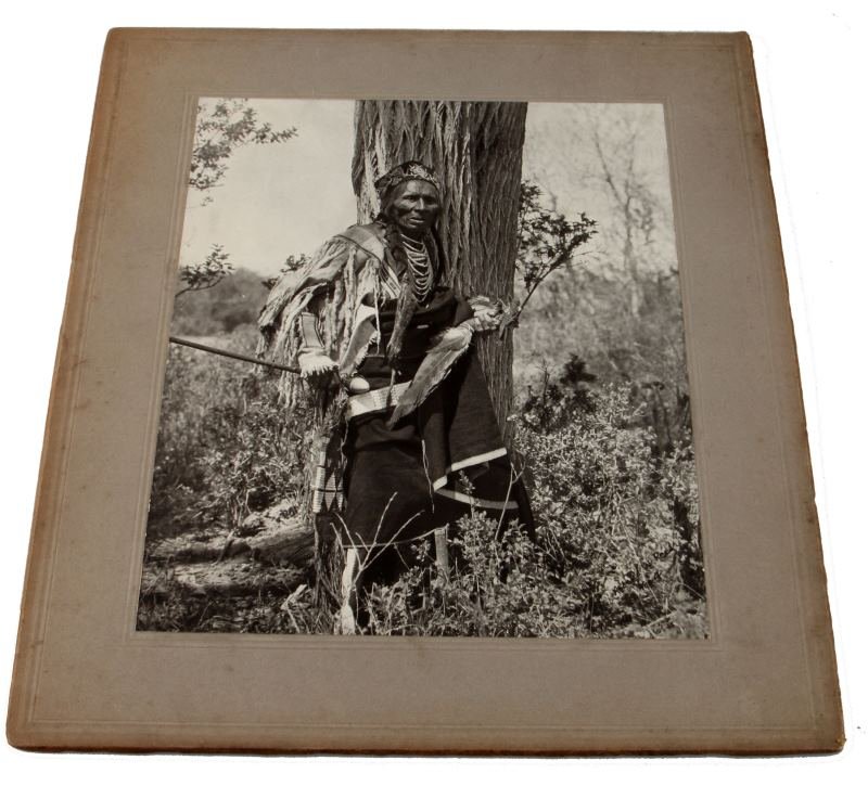 LARGE 8 X 10 INCH ROLAND W. REED 1904 INDIAN PHOTO: Stunning photograph of old warrior in battle dress with skull cracker in hand. named to Roland W. Reed lower right corner. Measures 14 by 12.