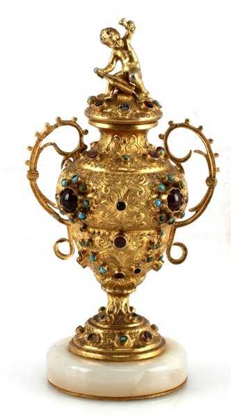ANTQUE BACCHIC JEWELED BRASS AMPHORA 5.25 IN TALL: A 5.25 inch brass amphora decorated with various jewels and stones. The lid is decorated with an infant Bacchus straddling a bottle of wine and raising a goblet. Stands on a marble base. In very good