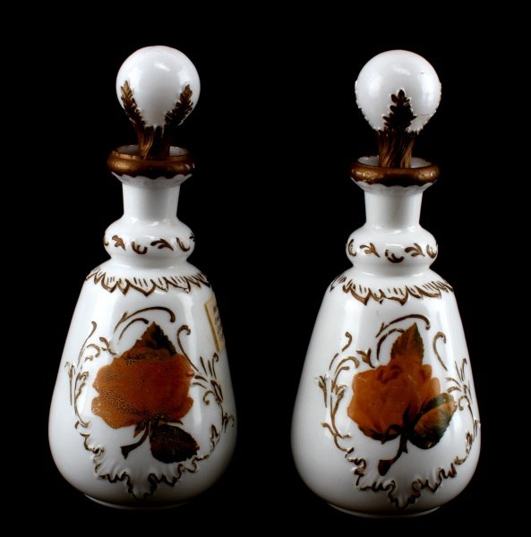 LOT OF 2 MATCHING BARBER BOTTLES WITH STOPPERS: Milk glass hand painted. Each piece has a leave on the front. There is a floral pattern around the top.