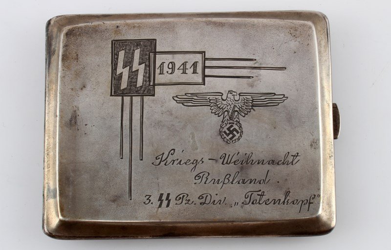 WWII THIRD REICH SS PANZER DIVISION CIGARETTE CASE: A cigarette case engraved with an image of a soldier carrying a pine tree with a caption reading "Weihnachten im Osten" (Christmas in the East) on the obverse and SS runes and eagle plus a commemorati