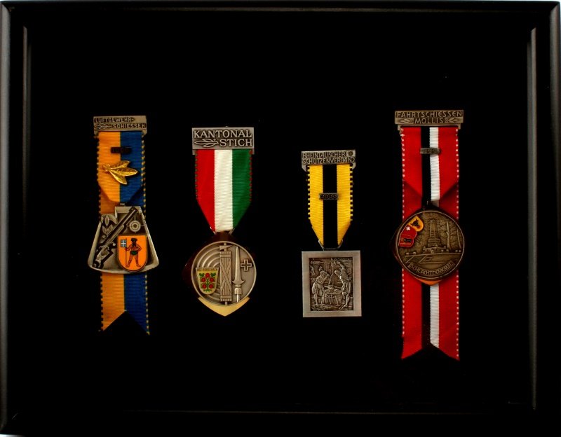 VINTAGE SWISS SHOOTING MEDAL LOT OF 4 IN CASE: Lot of four vintage Swiss medals awarded for marksmanship, shootings, and other activities. Three badges are dated: 1986, 1991, and 2000. Placed in wooden shadow box measuring 13 by 10.25 inches. Ther