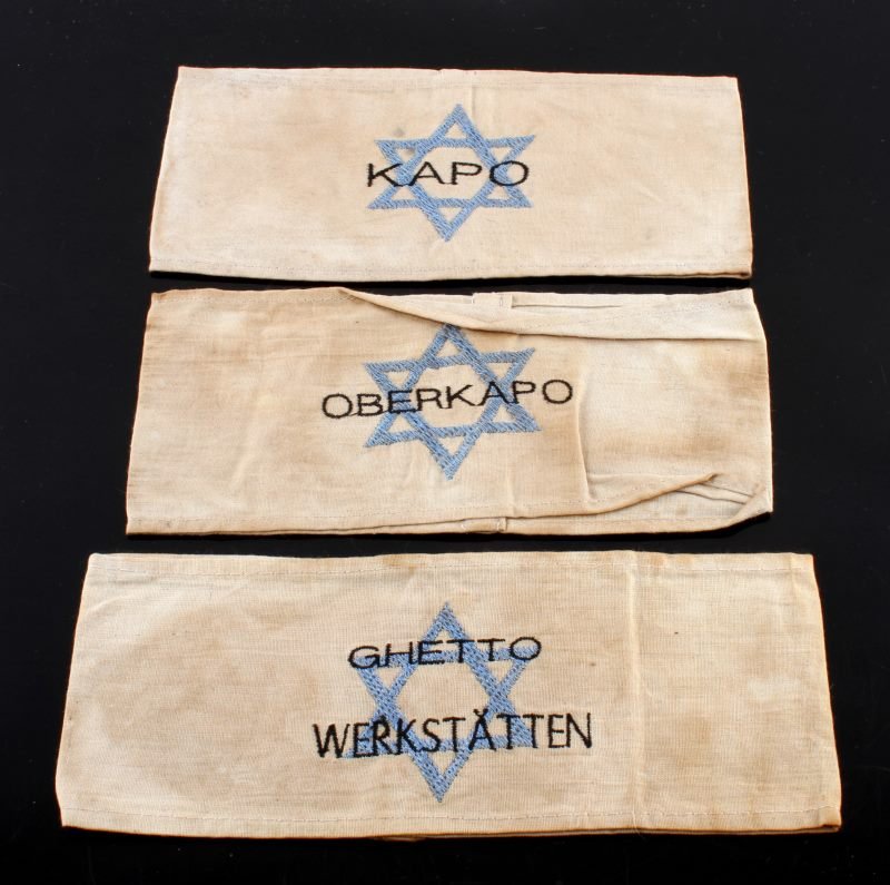 LOT OF THREE WORLD WAR II STAR OF DAVID ARMBAND: Three total armbands, all white with a blue star of David. One says "GHETTO WERKSTATTEN," one says, "KAPO," one says, " OBERKAPO." All have little to no fraying of fabric and are entirely intact. Item