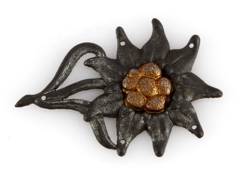 WWII THIRD REICH GERMAN EDELWEISS HAT BADGE: An edelweiss cap badge as worn by Third Reich German mountain troops. In good condition with some patina. Two piece construction. Has five holes for attaching to a cap.