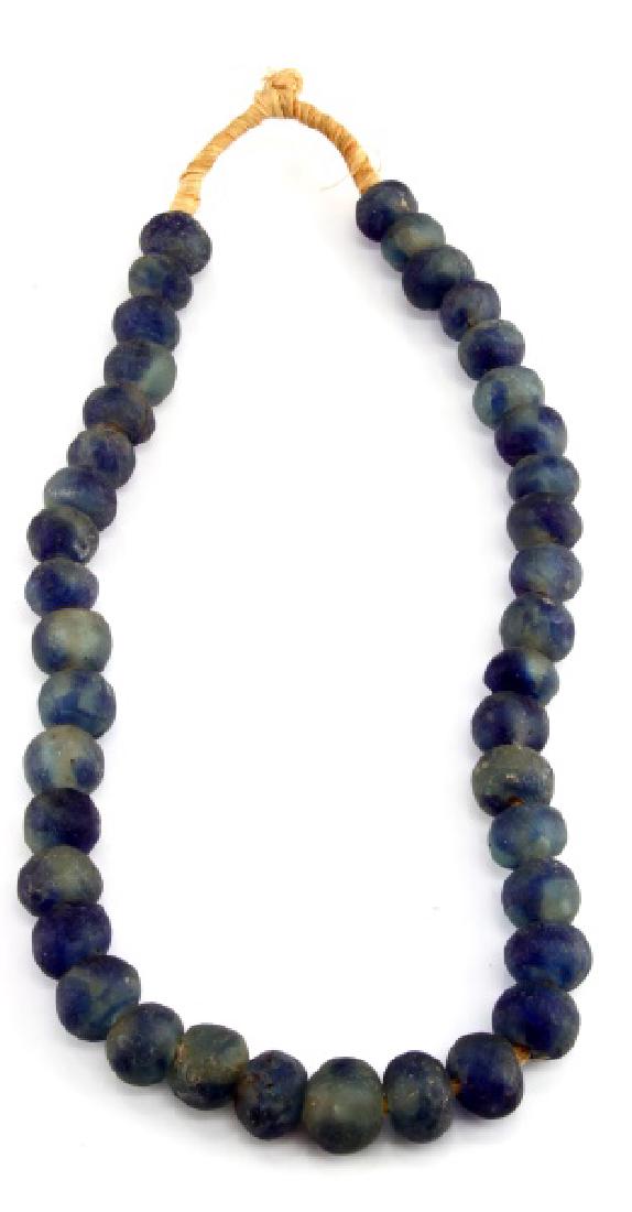 COBALT BLUE GROUND GLASS SPHERICAL TRADE BEADS: A strand of 40 roughly spherical, ground cobalt blue glass trade beads. Beads of this type were manufactured in Russia and Central Europe and used extensively in the Americas as trade items with vario