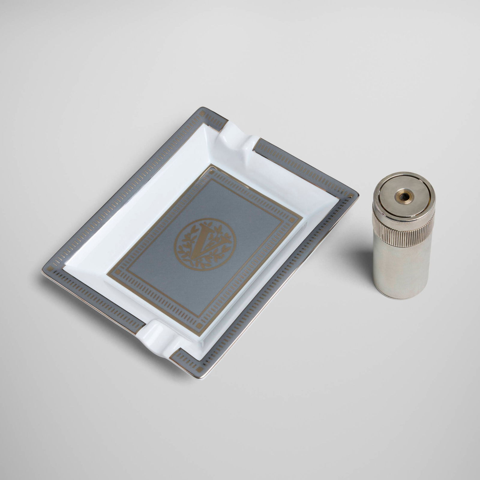 S.T. Dupont, Cylindrique table lighter and Place Vendome ashtray: S.T. Dupont Cylindrique table lighter and Place Vendome ashtray France, c. 1980, 2008silver-plated metal, glazed porcelain lighter: 4.375 h x 1.625 dia in (11 x 4 cm) ashtray: 1.25 h x 6.375 w x 7