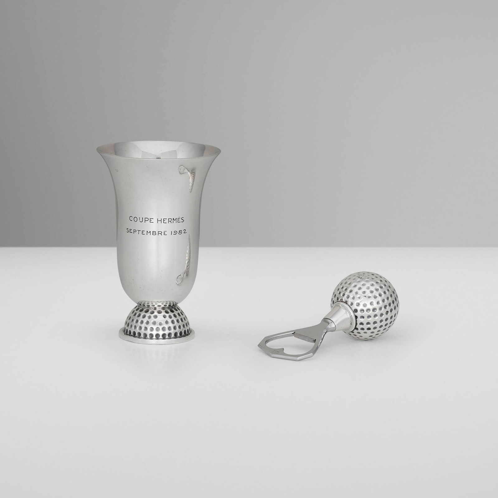 Hermes, Golf Ball coupe and bottle opener: Hermes Golf Ball coupe and bottle opener Ravinet d'Enfert & Cie France, c. 1965-1982 silver-plated metal, stainless steel 4.25 h x 2.75 dia in (11 x 7 cm) 3.75 h x 1.5 dia in (10 x 4 cm) Impressed