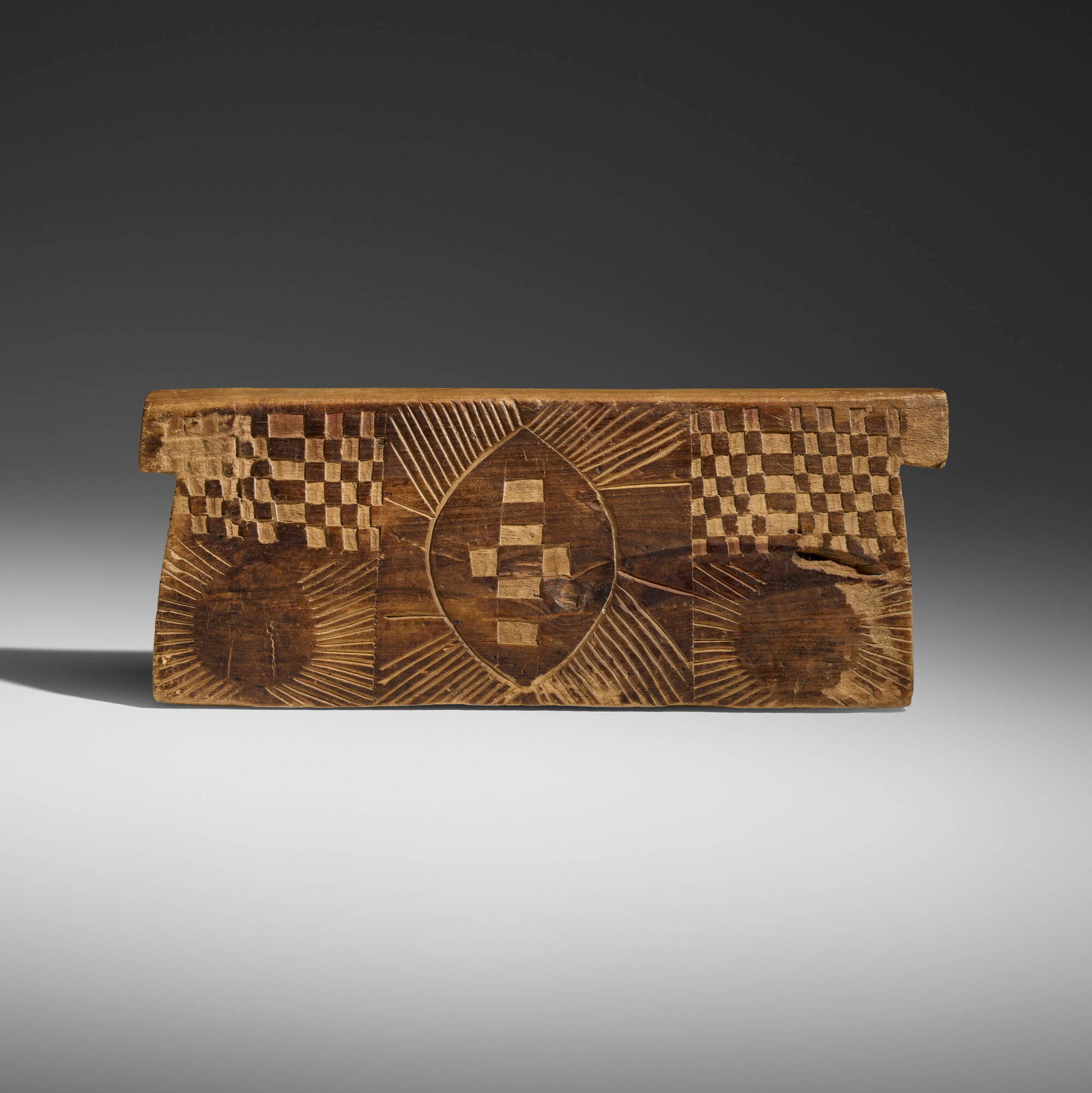 Zulu, Headrest: Zulu Headrest South Africa, 20th century carved wood 7 h x 18 w x 3.5 d in (18 x 46 x 9 cm) This headrest features motifs of a warrior's shield, cross, checkerboard, and sunbeam designs.
