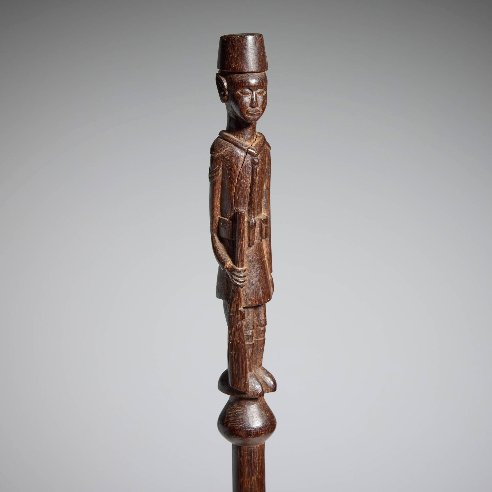 Kamba, Askari staff: Kamba Askari staff Kenya, 20th century carved wood 38.5 h x 1 dia in (98 x 3 cm) This ebony staff is surmounted by a finial figure wearing the uniform and fez of the King's African Rifles. This work