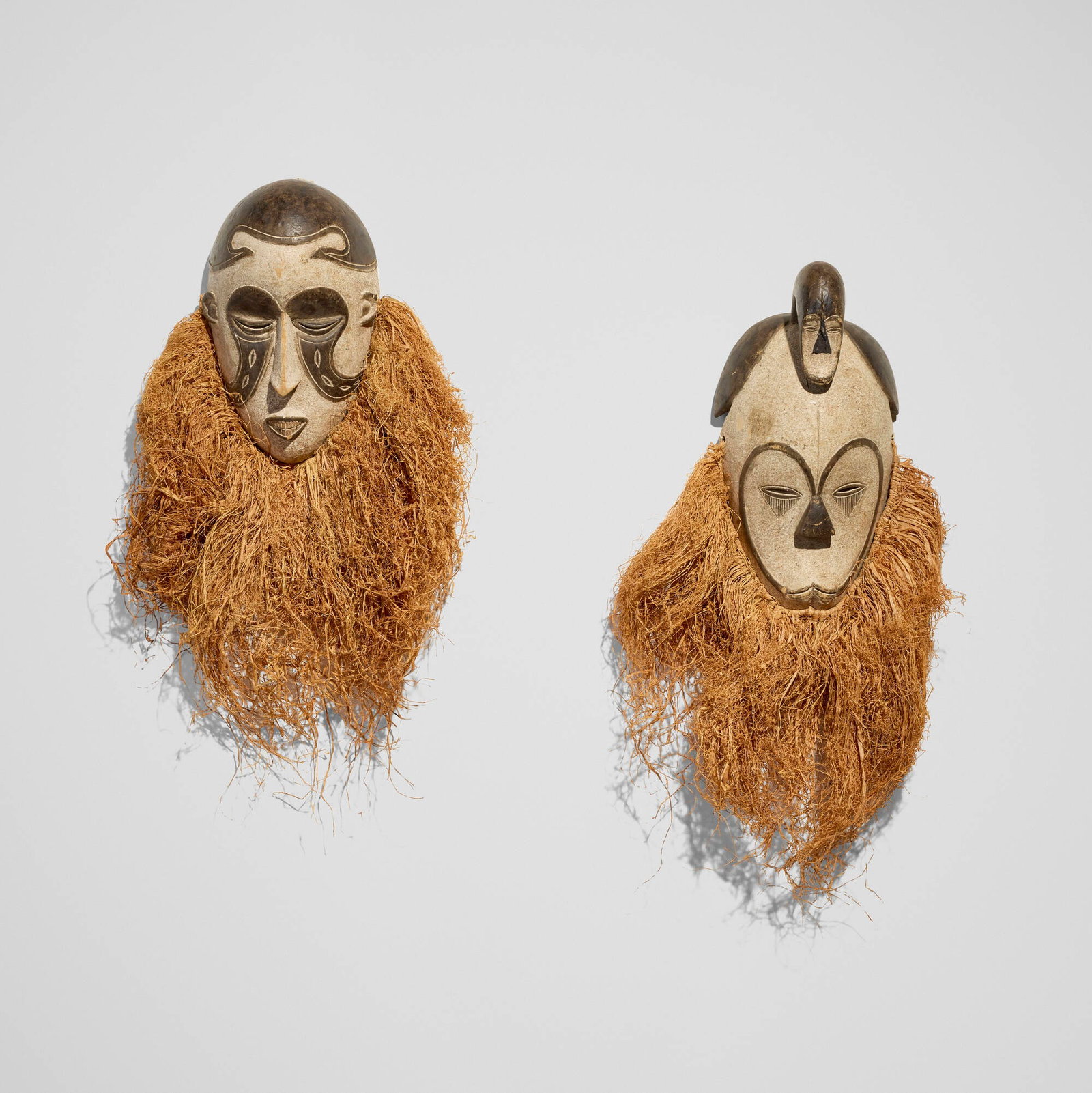 Gabonese, Masks, set of two: Gabonese Masks, set of two late 20th century carved and painted wood, raffia 27 h x 14 w x 5 d in (69 x 36 x 13 cm) 24 h x 14 w x 5 d in (61 x 36 x 13 cm) Provenance: The Sam and Beverly Maloof