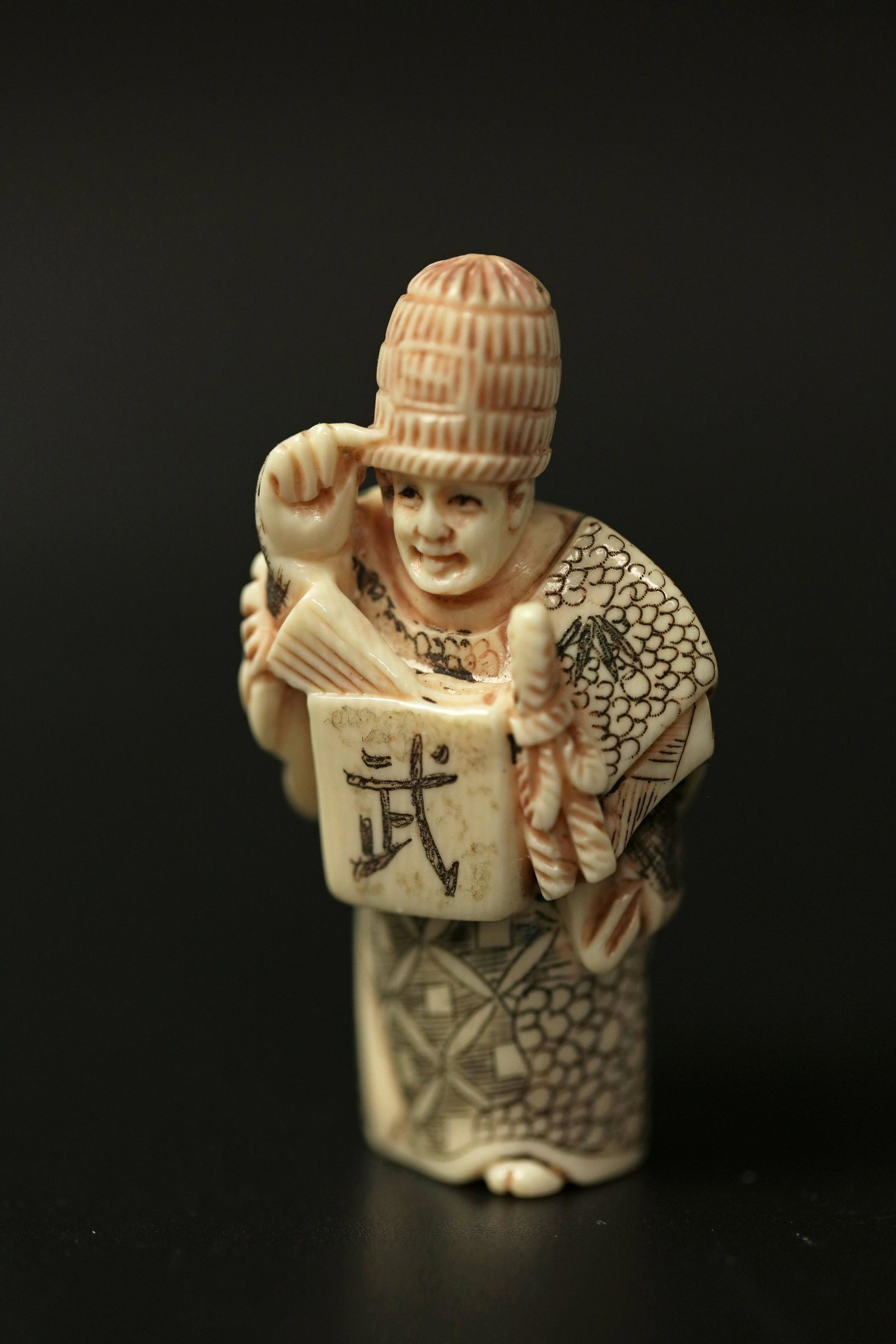 A Netsuke Miniature Carved Bone Sculpture of an: A Netsuke Miniature Carved Bone Sculpture of an Official Holding a Chinese Sign. H: 2.25 in. (5.72 cm) W: 1.25 in. (3.18 cm) D: 0.8 in. (2.03 cm)