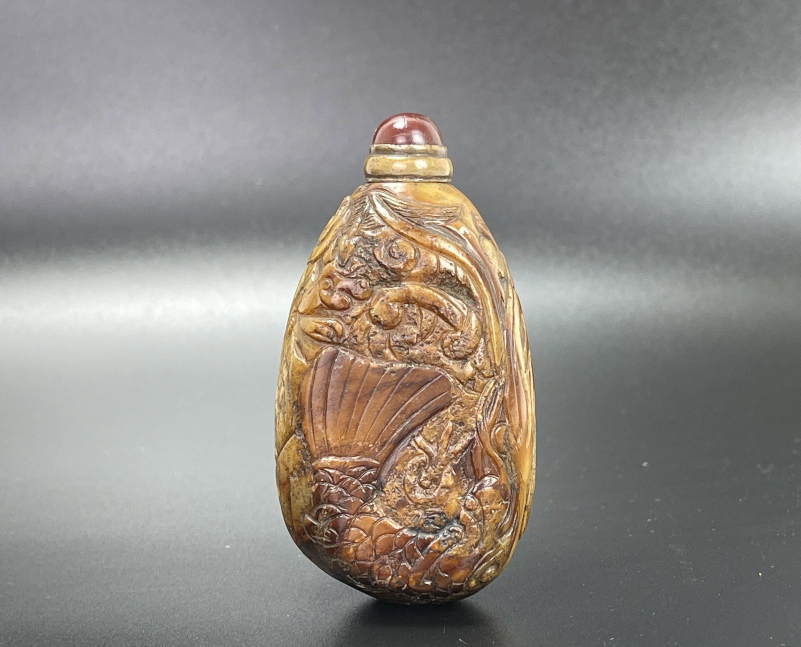 Flattened Pebble-shape Soapstone Snuff Bottle: Flattened Pebble-shape Soapstone Snuff Bottle, H 8.5 cm(3.4 in.),China, carved with a jumping carp amongst auspicious clouds with a flaming pearl, well hollowed, brass stopper topped with domed crimso
