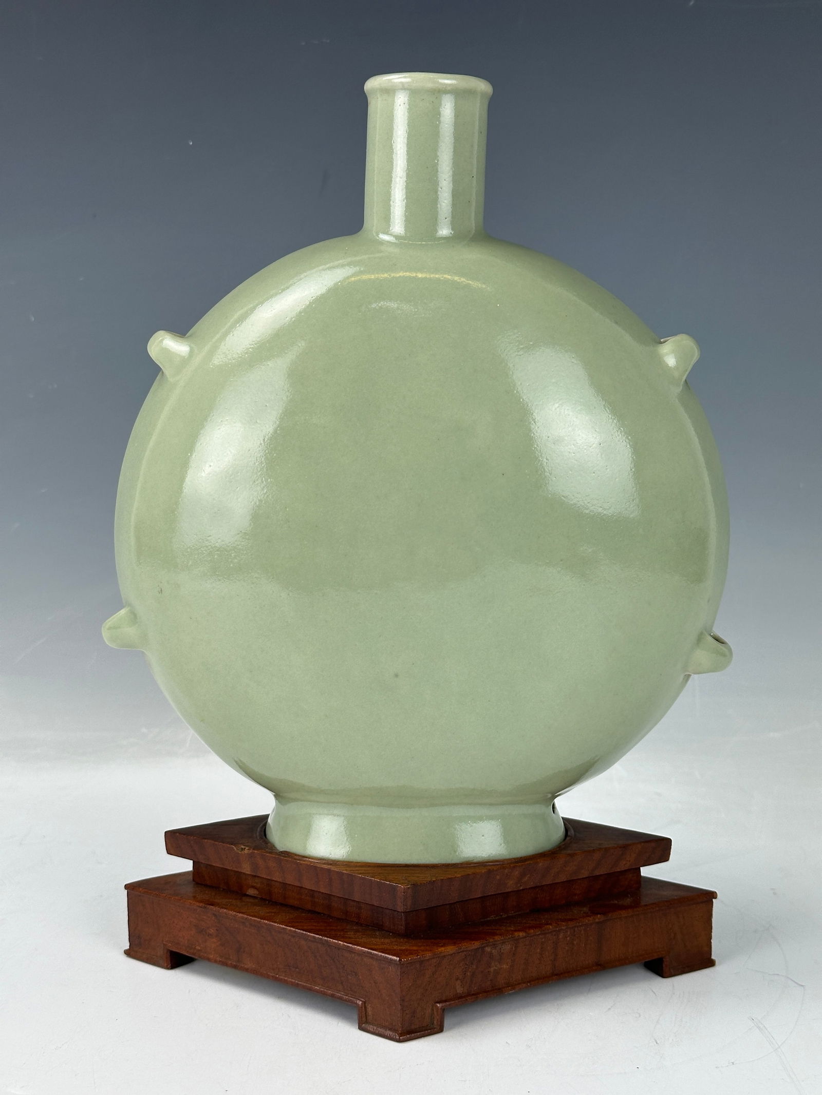 A Chinese Celadon Glazed Porcelain Flask Vase: A Chinese Celadon Glazed Porcelain Flask Vase, with wood base,H23cm. Preview from Jun. 24th to 28th from 1:00 PM TO 5:00 PM Eastern Time, Location: 15229 Display Court, Rockville MD 20850.