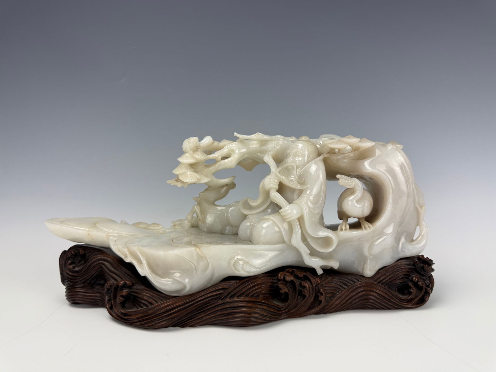 Chinese White Jade Carving Immortal on a Raft with Wood stand: a Chinese white jade carving depicting an immortal on a raft, with fitting wood stand.H 35cm (14in) x W 16cm (6.5in) x D 11cm (4.5in) .Preview from Feb 23rd to 27th from 1:00 PM TO 5:00 PM Eastern Tim