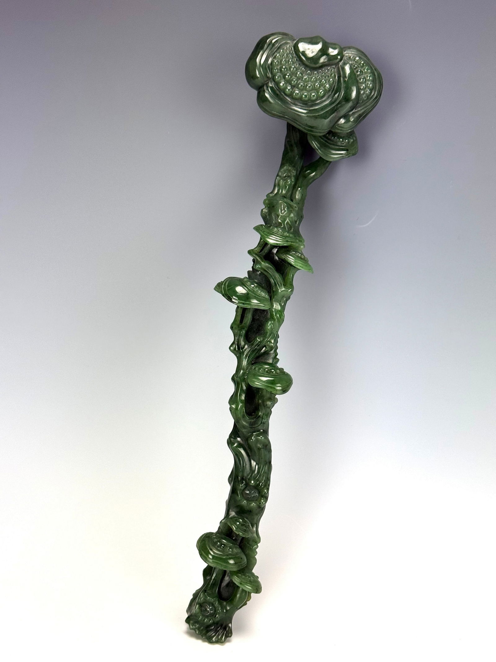 A Green Hetian Nephrite Lingzhi Form Ruyi Scepter: A traditional Chinese jade ruyi scepter, a ceremonial object often symbolizing power, good fortune, and longevity. W 34.5 cm(in) x H 8 cm(3 in) x D 5 cm(in 2 ).Preview from Apr 20th to 24th from 1:00