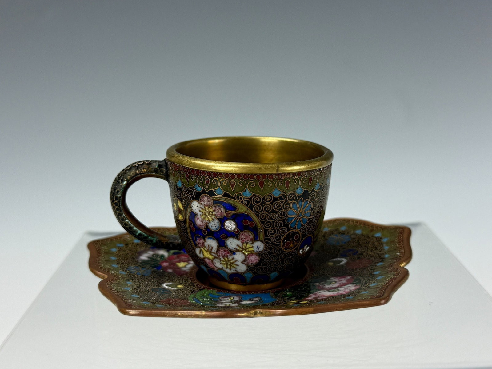 Chinese Cloisonne Enamel Cup and Saucer with Floral and Gilt Interior Decoration: Chinese Cloisonne Enamel Cup and Saucer with Floral and Gilt Interior Decoration. Sauce D 10 cm(4 in.),cup W 4 cm(1.6 in.),Preview from Aug 24th to 28th from 1:00 PM TO 5:00 PM Eastern Time, Location: