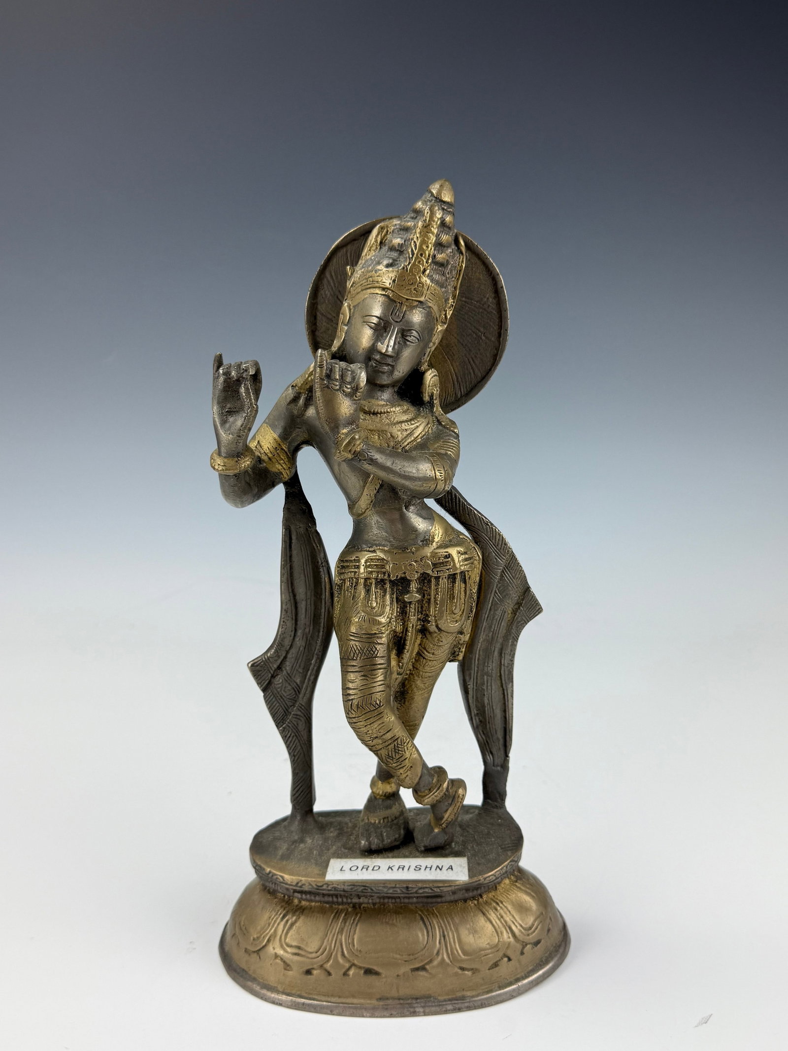 Vintage Brass Statue of Lord Krishna: Metal Statue of Lord Krishna with Halo and Engraved Base. H 28.5 cm(11.2 in.). Preview from Aug 24th to 28th from 1:00 PM TO 5:00 PM Eastern Time, Location: 15229 Display Court, Rockville, MD 20850.