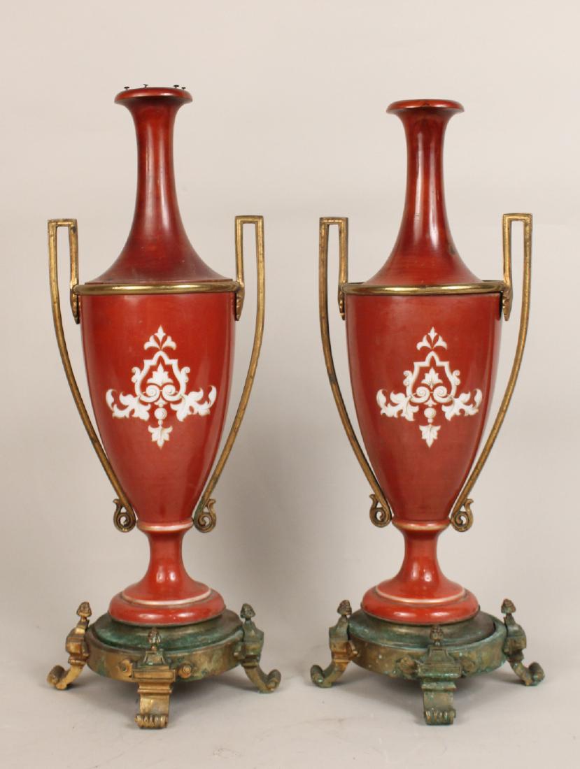 Pair of Red Porcelain Long Neck Amphora's: Depicting Greco-Roman figures with brass mounts and stands. 22"h x 7"d.